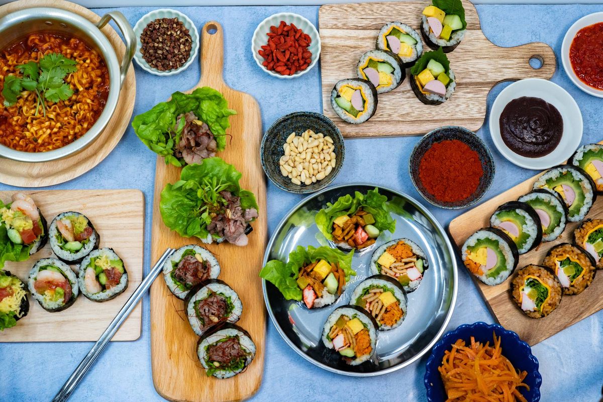青いテーブルに並ぶキンパ、サンチュ包み、ラーメン、薬味